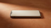 Modern smartphone with blank white screen lying flat on warm brown leather surface with soft natural lighting and shadows.