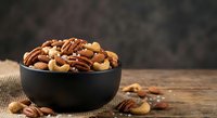 Mixed nuts assortment in black bowl on rustic wooden table with burlap texture, healthy snacking and cooking ingredient for recipes and meal preparation.