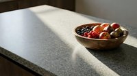 Wooden bowl filled with mixed olives and cherry tomatoes on gray countertop with natural sunlight, suitable for food styling and kitchen design projects.