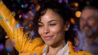 Young mixed race woman with curly hair smiling with eyes closed as colorful confetti falls around her, expressing joy and celebration against dark background.