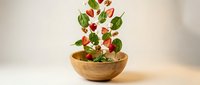 Fresh mixed salad leaves with cherry tomatoes floating and falling into wooden bowl on neutral background for healthy eating concepts.