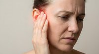 Woman experiencing ear pain, touching her inflamed ear with a worried expression, highlighting symptoms of infection or tinnitus.