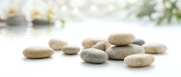 Smooth river stones and pebbles scattered on white surface with blurred spa elements in background, suitable for wellness, meditation, and relaxation design projects.