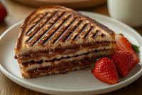 Grilled chocolate hazelnut sandwich with golden crispy bread served on white plate with fresh strawberries for breakfast or dessert menu.