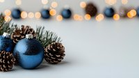 Blue glittery Christmas ornament with natural pine cones and evergreen branches against blurred warm bokeh lights background creating festive holiday atmosphere.