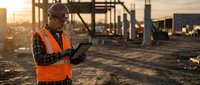 African American construction worker using digital tablet at building site during golden hour sunset for project management and safety inspection.