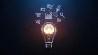 Glowing light bulb with digital business icons floating above on dark background representing innovation and creative marketing solutions.