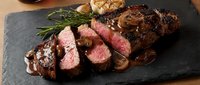 Grilled beef steak sliced medium-rare with mushroom sauce and rosemary garnish on dark slate board, perfect for restaurant menus and culinary presentations.