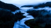 Mystical river landscape at dawn with low-lying fog weaving through forested mountains, creating ethereal atmosphere. Meandering waterway reflects moody blue light.