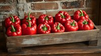 Fresh red bell peppers arranged in rustic wooden crate against brick wall background, bright glossy vegetables with green stems showcase farm fresh produce.
