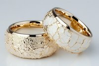 Two elegant gold wedding rings with textured cracked surface pattern isolated on white background. Luxury jewelry bands for marriage ceremony and engagement.