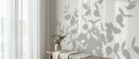 Soft botanical leaf shadows on a white wall with sheer curtains, wooden bench, and dried flowers in a vase, minimal Scandinavian interior.