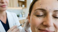 Professional cosmetic surgeon marking facial injection points on relaxed Caucasian woman patient before aesthetic treatment procedure in modern clinic.