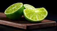 Fresh cut lime halves with juicy pulp and bright green flesh on dark wooden cutting board against black background, dramatic lighting highlights citrus texture.