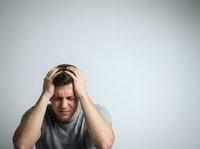 Stressed man with hands on head wearing gray t-shirt against white background, expressing frustration, anxiety, headache, or mental exhaustion for wellness and health concepts.