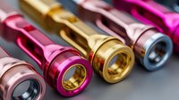 Colorful metallic fishing reel parts in gold, pink, and red arranged in row on gray background, showcasing precision engineering for sport fishing equipment.