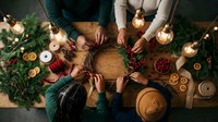 Overhead view of family hands reaching across festive holiday table with Christmas decorations, candles, and seasonal treats creating warm gathering atmosphere.