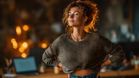Young woman with curly hair wearing cozy knit sweater relaxing with eyes closed in warm evening light. Peaceful moment of self-care and mindfulness at home.