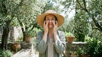 Woman in straw hat calling out in lush garden with olive trees and terracotta pots, suitable for lifestyle, communication, and outdoor advertising campaigns.