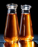Two glass bottles filled with amber liquid against dark background, isolated for beverage packaging and advertising design use.