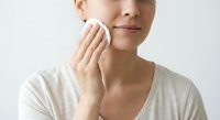 Young woman applying skincare product with cotton pad on face for daily beauty routine and facial cleansing regimen.