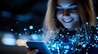 Young woman with blonde hair smiling at glowing smartphone screen in dark room with magical blue light effects and bokeh particles creating ethereal atmosphere.
