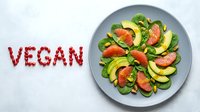 Fresh vegan salad with grapefruit, avocado, spinach, and pistachios on a plate, with the word vegan spelled in pomegranate seeds on a light background.
