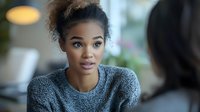 Young African American woman in gray sweater listening intently during conversation at cafe, natural lighting and soft bokeh background creates professional atmosphere.
