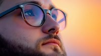 Close up portrait of bearded caucasian man wearing glasses looking up thoughtfully against warm sunset sky background, side view profile showing contemplative expression.