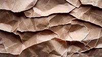 Crumpled brown kraft paper background with natural folds and wrinkles creating abstract textural pattern. Rough recycled material surface in sepia tones.