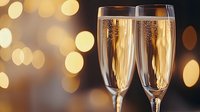Two champagne flutes filled with golden sparkling wine against warm bokeh lights background for celebration and festive occasions.