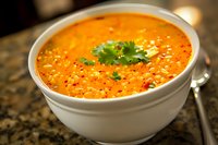 Creamy orange carrot soup garnished with fresh cilantro and black pepper in white ceramic bowl, selective focus on vibrant homemade vegetable puree.