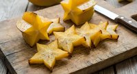 Fresh star fruit slices on wooden cutting board with knife, tropical carambola pieces ready for healthy snacking and culinary preparation.