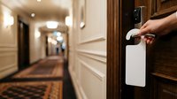 Person placing do not disturb sign on hotel room door handle in corridor with warm lighting and wooden trim.