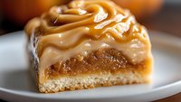 Decadent caramel dessert bar with layers of shortbread crust, gooey caramel filling and swirled cream topping served on white plate, macro food photography.