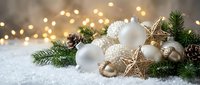 White and gold ornaments with evergreen branches and star decorations arranged on snow, featuring warm bokeh lights in background for festive holiday and seasonal celebrations.