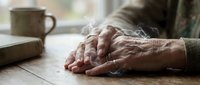Elderly hands resting on wooden table with coffee mug, showcasing aging, wisdom and peaceful moments in senior lifestyle and retirement years.