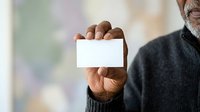 Mature man with dark skin tone holding blank white business card in hand, wearing dark sweater, suitable for corporate identity, networking, and professional branding projects.