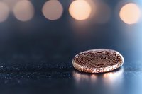 Cryptocurrency coin on dark surface with bokeh lights background, macro shot showing detailed texture and metallic reflection in warm golden tones.