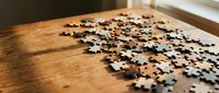 Scattered jigsaw puzzle pieces on wooden table surface creating engaging brain teaser and problem-solving activity for leisure time entertainment.