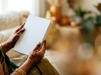 Hands holding blank white book or journal with henna decorated fingers, warm home interior background with bokeh lighting for publishing and lifestyle content.