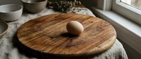 Single brown egg on rustic wooden cutting board in modern kitchen setting with natural lighting and cooking utensils for culinary preparation.