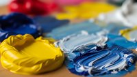 Vibrant acrylic paint palette with yellow and blue colors mixed on artist surface for creative painting projects and artistic expression.