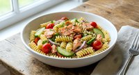 Fresh pasta salad with grilled chicken, cherry tomatoes, avocado and herbs in white bowl on wooden table. Healthy Mediterranean lunch meal for summer dining.