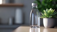 Empty transparent glass bottle with screw cap next to small potted succulent plant on wooden surface against blurred kitchen background, minimalist style.