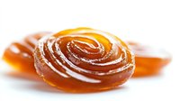Amber caramel candy with swirl pattern dusted with sugar, isolated on white background. Sweet hard candy for confectionery and food design use.
