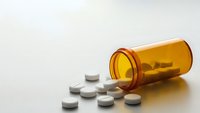 Amber prescription bottle with white pills spilled out on clean surface for medical healthcare and pharmaceutical concepts.