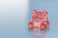 Pink gummy bear candy on a light blue reflective surface, soft studio lighting, sweet treat concept for food and confectionery projects.