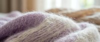 Soft knitted wool blanket in purple and beige tones creating cozy home comfort atmosphere for relaxation and warmth during cold seasons.