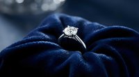 Elegant diamond engagement ring with brilliant cut stone on luxurious navy blue velvet fabric background for wedding and jewelry concepts.
